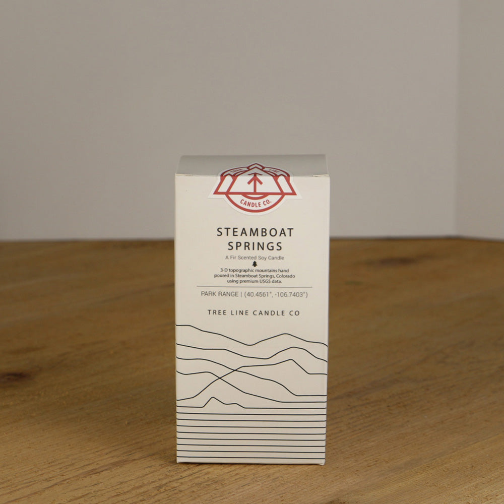 A white wax replica candle of Steamboat Springs summit next to a white box with red and black lettering.