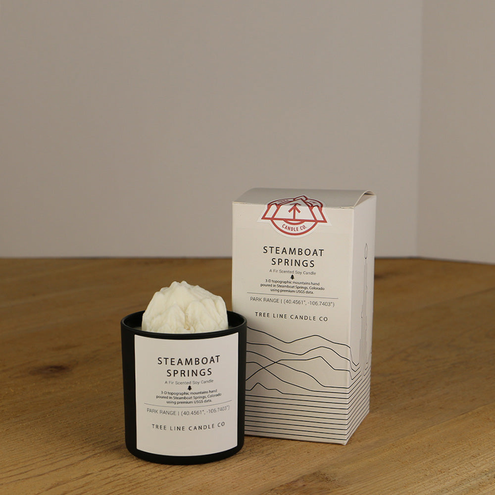 A white wax replica candle of Steamboat Springs summit next to a white box with red and black lettering.