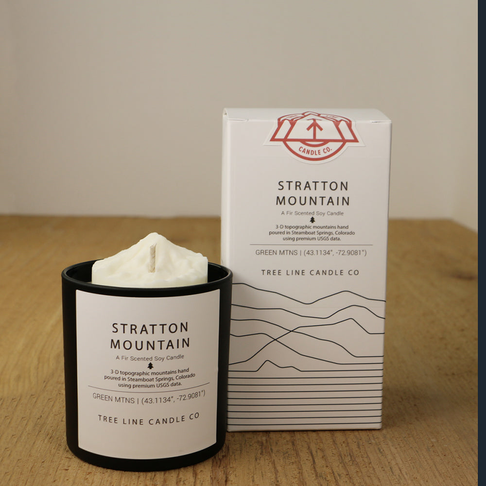 A white wax candle named Stratton Mountain is next to a white box with red and black lettering.