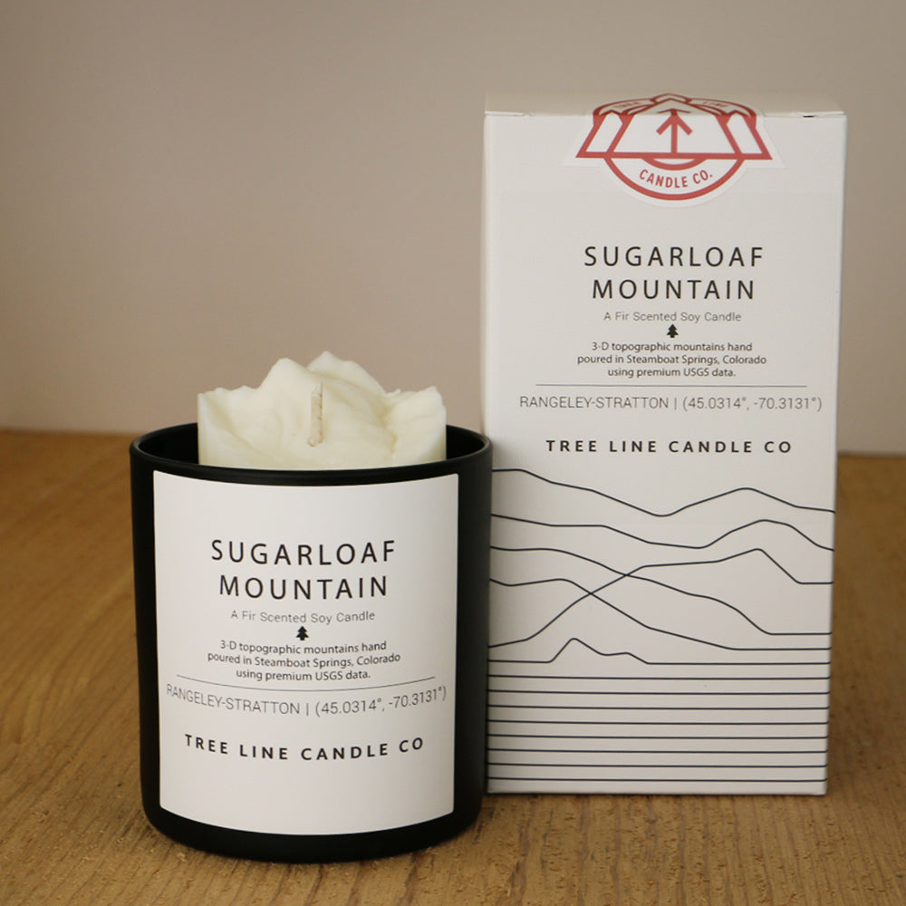 A white wax candle named Sugarloaf Mountain is next to a white box with red and black lettering.