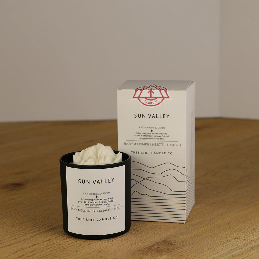 A white wax replica candle of Sun Valley summit next to a white box with red and black lettering.