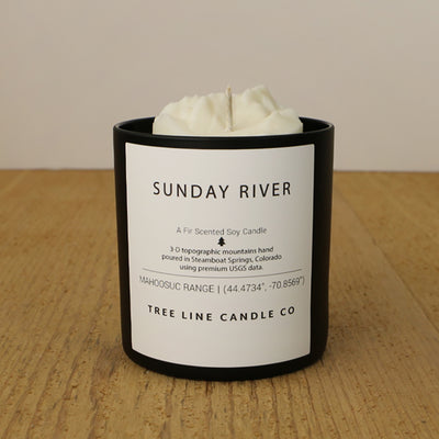  A white soy wax replica candle of Sunday River in a round, black glass.