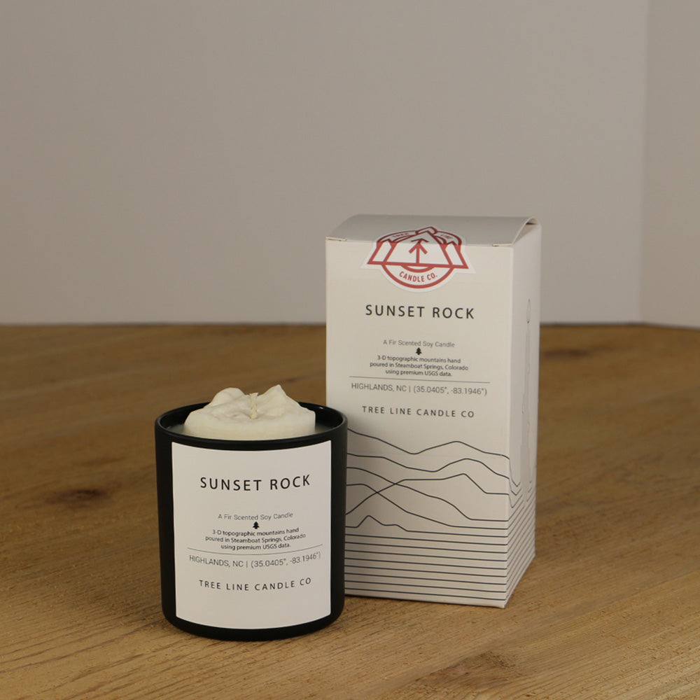 A white wax replica candle of Sunset Rock  next to a white box with red and black lettering.