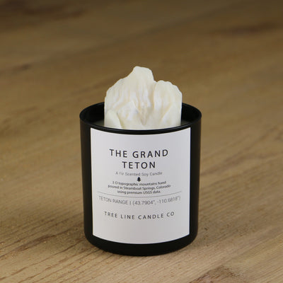  A white soy wax replica candle of The Grand Teton mountains  in a round, black glass.