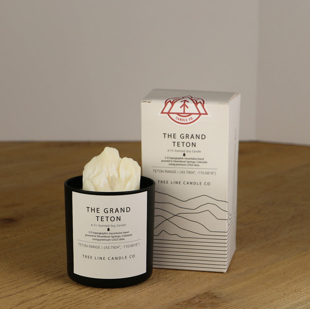 A white wax replica candle of The Grand Teton next to a white box with red and black lettering.