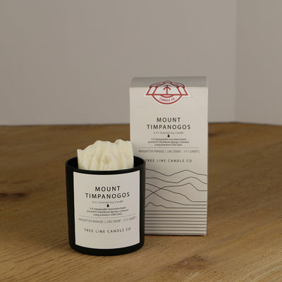 A white wax replica candle of Mount Timpanogos next to a white box with red and black lettering.