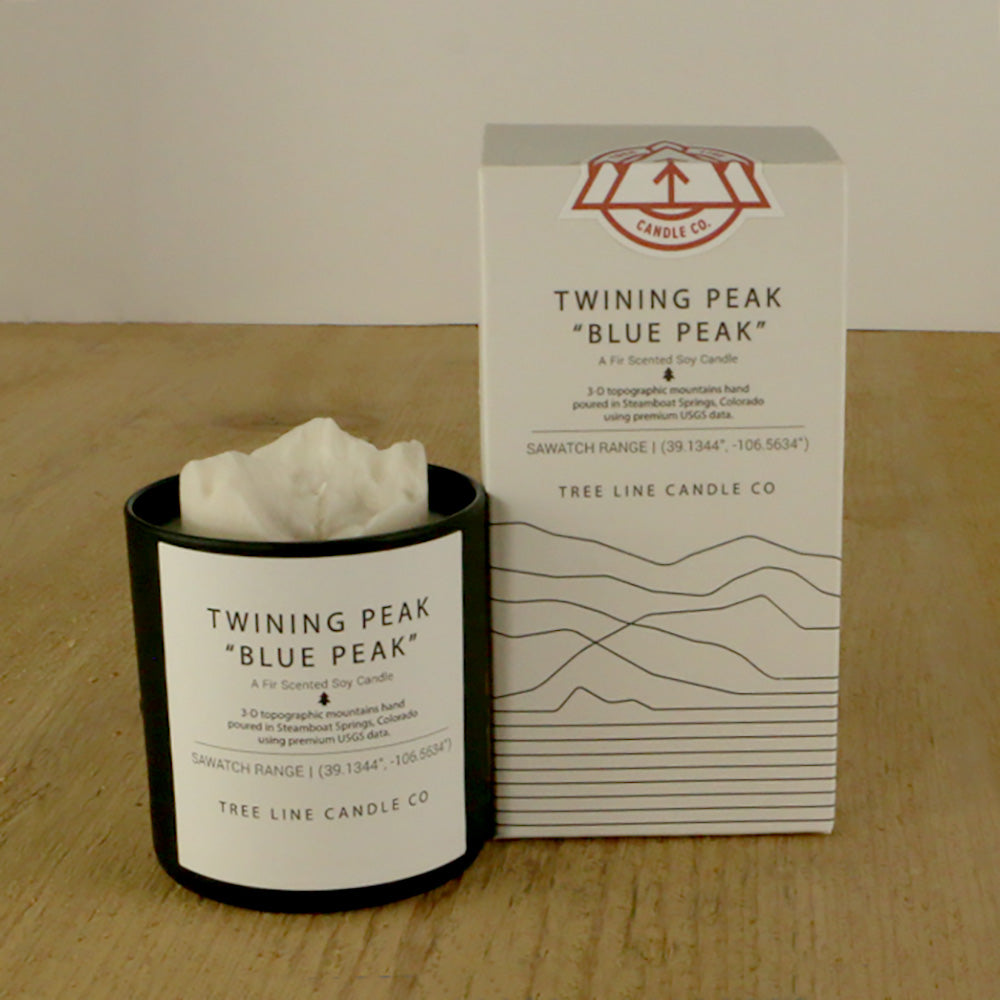 A white wax candle named Twining Peak is next to a white box with red and black lettering.