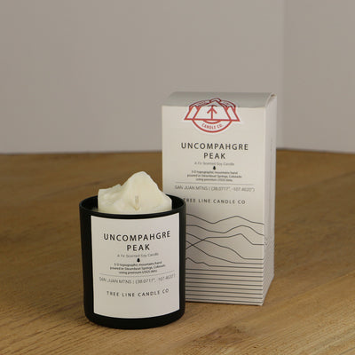 A white wax replica candle of Uncompahgre Peak next to a white box with red and black lettering.