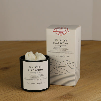 A white wax replica candle of Whistler Blackcomb next to a white box with red and black lettering.