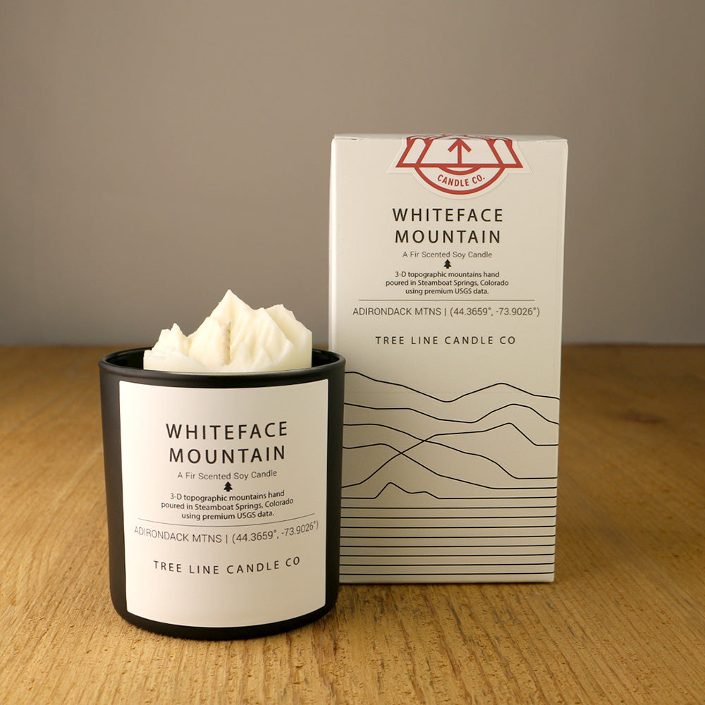 A white wax candle named Whiteface Mountain is next to a white box with red and black lettering.