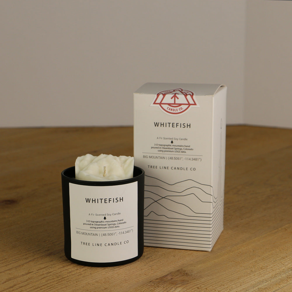 A white wax replica candle of Whitefish summit next to a white box with red and black lettering.