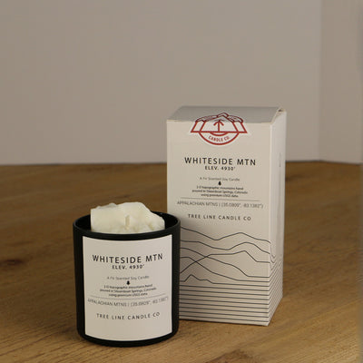 A white wax replica candle of Whiteside Mountain next to a white box with red and black lettering.