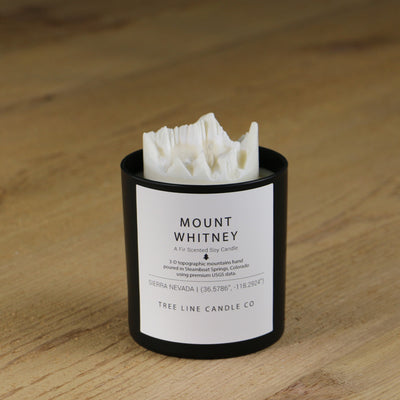 A white soy wax replica candle of Mount Whitney in a round, black glass.