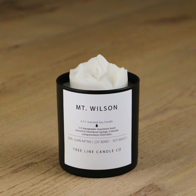 A white soy wax replica candle of Mt. Wilson in a round, black glass.