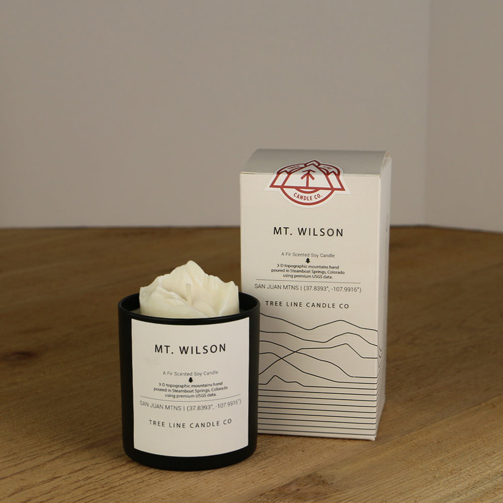 A white wax replica candle of Mount Wilson next to a white box with red and black lettering.